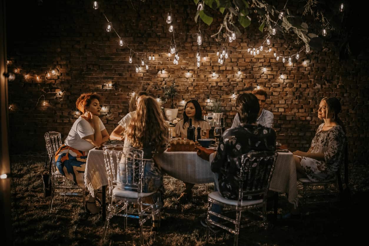 Outdoor dinner gathering with string lights in a backyard.