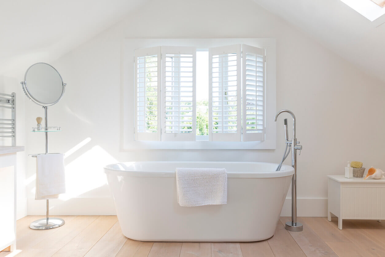 Bright bathroom with a freestanding bathtub and white plantation shutters allowing soft natural light.