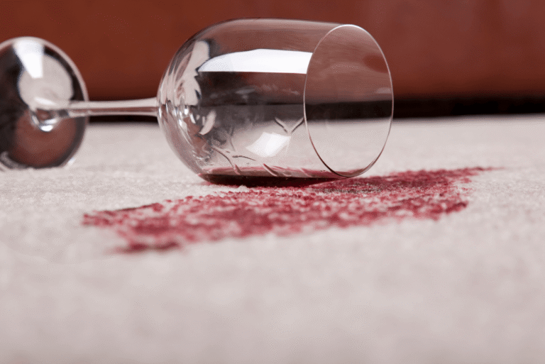 A wine glass spilled on a carpet floor.