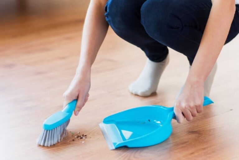 Close up of someone sweeping the floor with a hand broom.