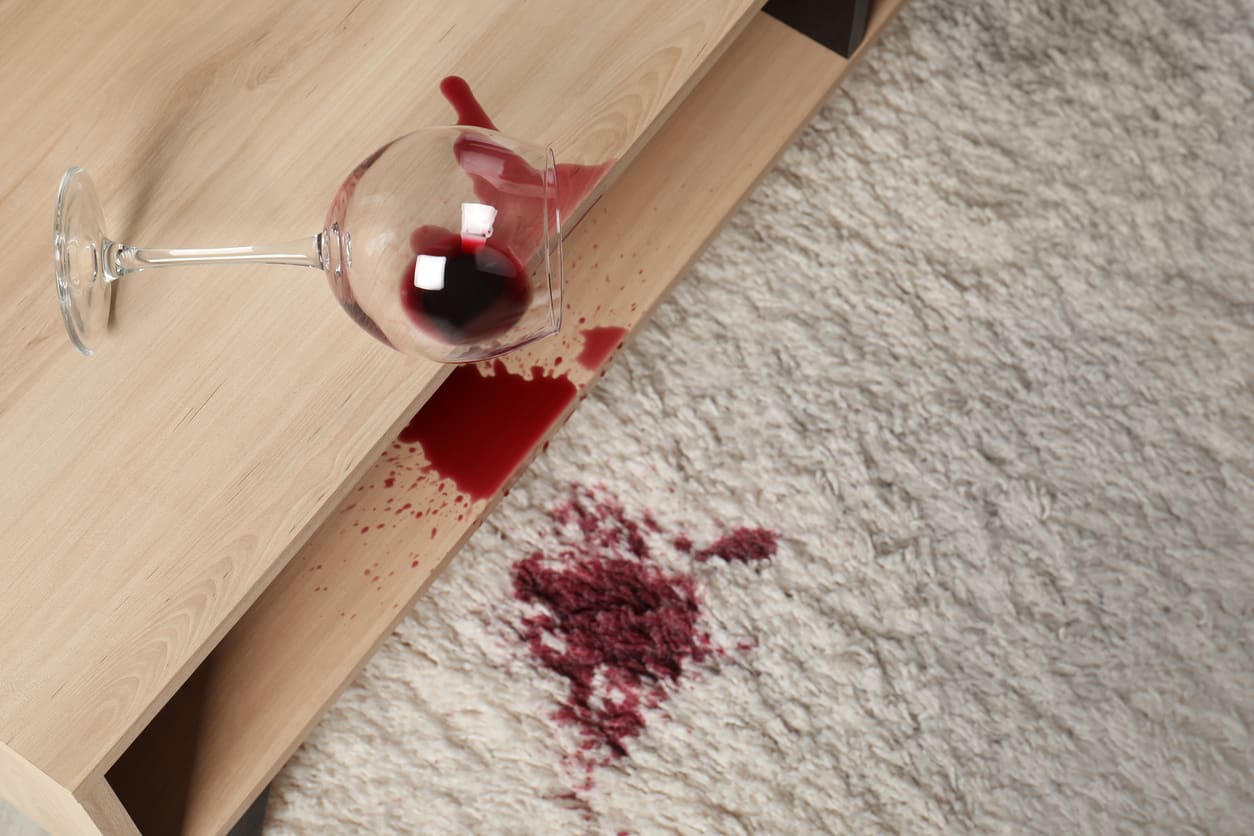 Spilled red wine leaving a dark stain on a light-coloured carpet.