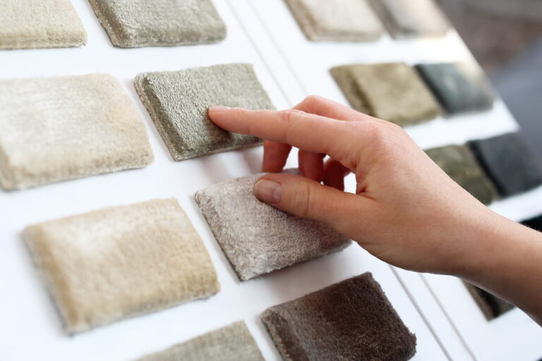 Hand touching and comparing carpet sample swatches displayed on a showroom board.