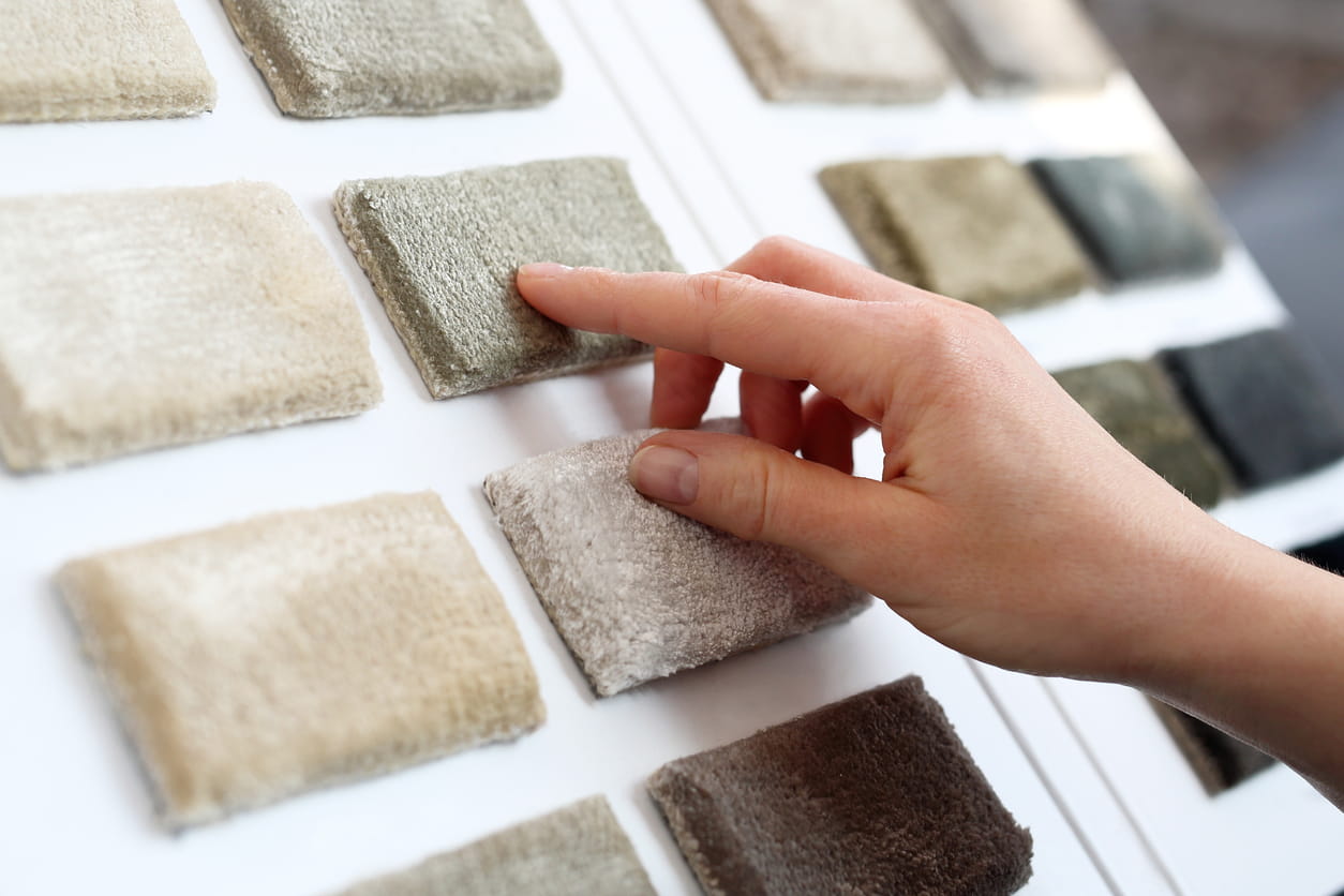 Hand touching and comparing carpet sample swatches displayed on a showroom board.