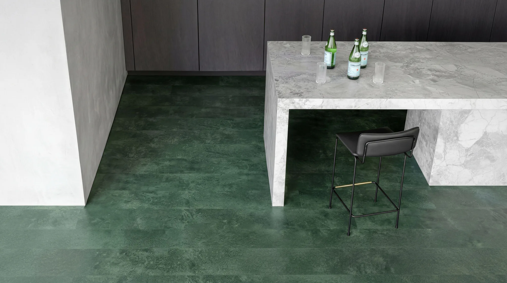 Contemporary bar interior featuring polished green concrete flooring, grey cabinetry, marble countertop with beer bottles and glasses, and black bar stool seating
