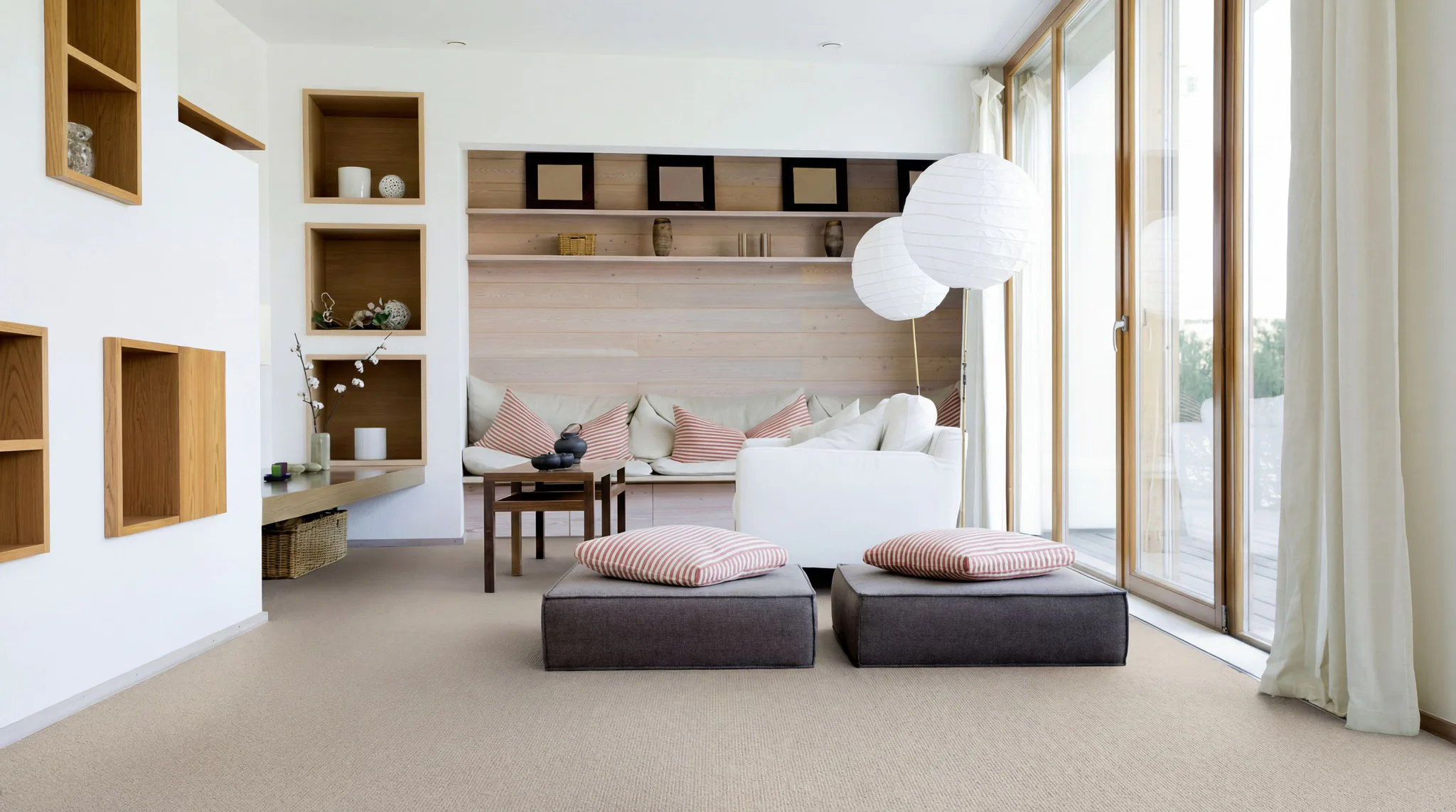 Contemporary living room featuring light beige sheet vinyl flooring, wooden built-in shelving, white paper pendant lights, striped accent pillows, and floor-to-ceiling glass doors overlooking outdo...