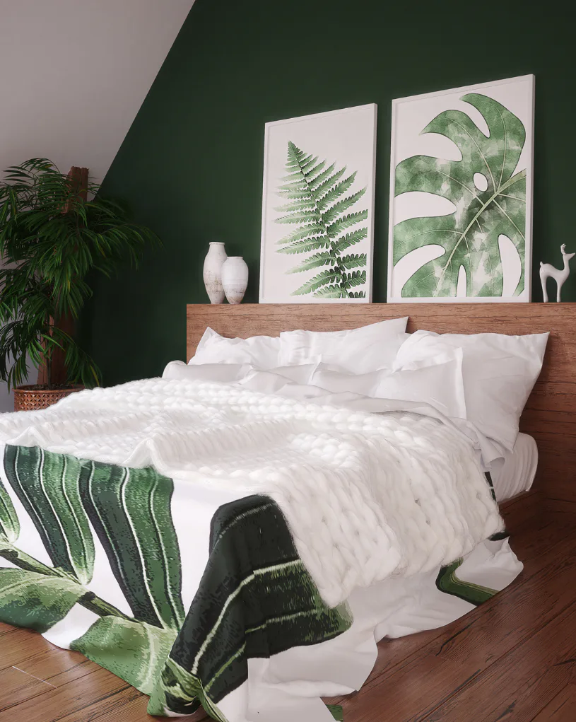 Modern bedroom with deep green accent wall, wood headboard with white bedding, two framed botanical prints of ferns and monstera leaves, white ceramic vases, potted plant, and green striped throw b...