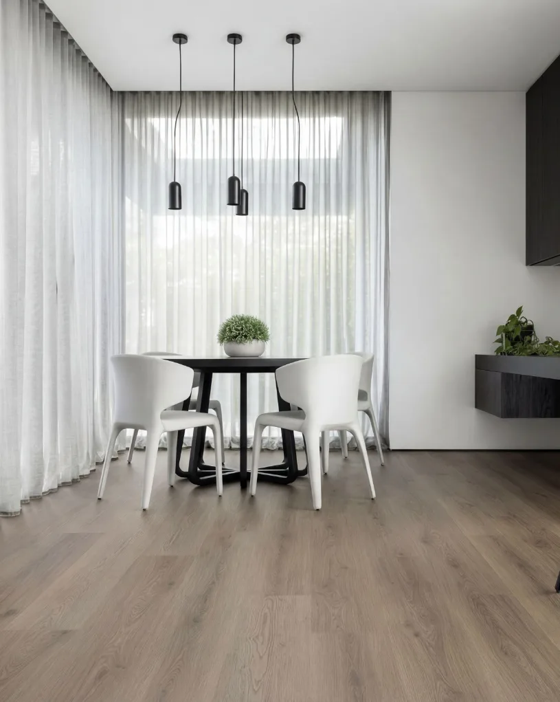Contemporary dining room featuring a black round table with four white chairs, three black pendant lights, and large windows with sheer curtains overlooking light wood flooring