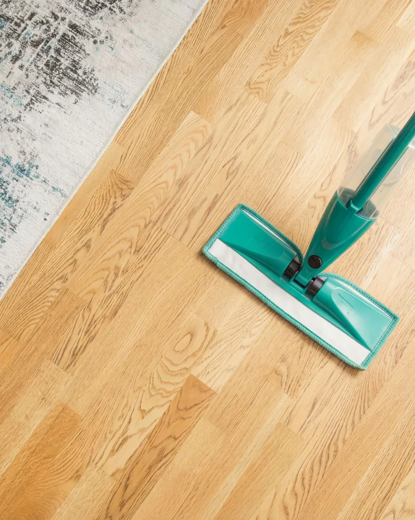 Turquoise microfiber mop with extendable handle cleaning a light wood floor next to white distressed flooring, showing effective hard floor cleaning technique.