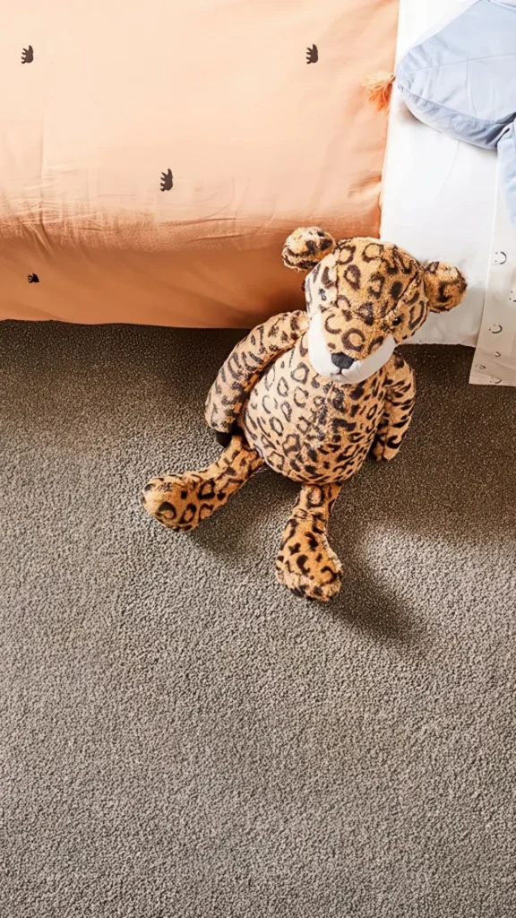 Leopard-patterned plush toy sitting on soft gray carpet next to colorful bedding, demonstrating carpet's comfort and durability for active family living.