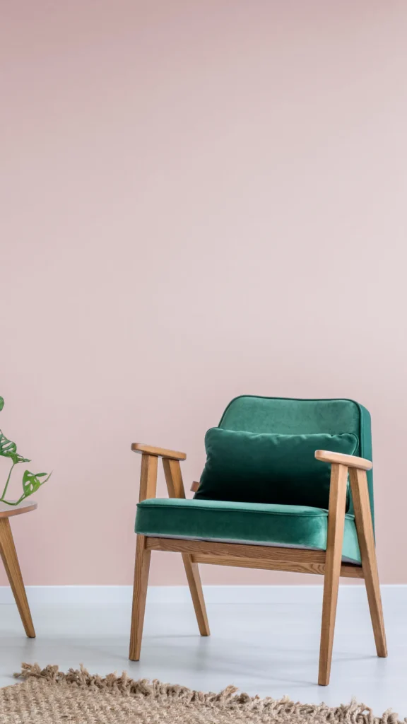 Teal velvet armchair with wooden frame and legs against pink wall, featuring clean mid-century modern lines and design, paired with potted plant and woven rug.