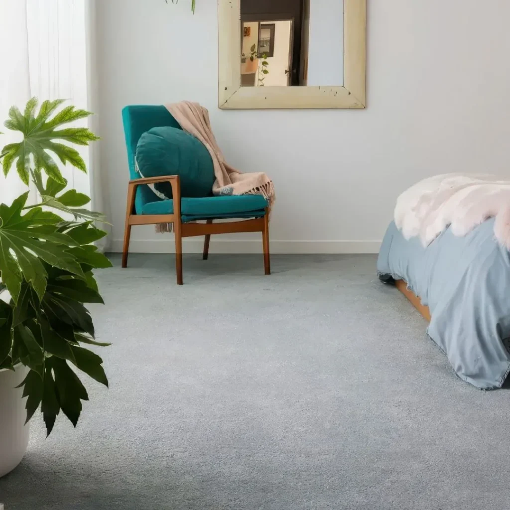 Modern bedroom featuring a teal upholstered mid-century chair with wooden frame on light gray Desire carpet, alongside a bed and potted green plant by a window with mirror.