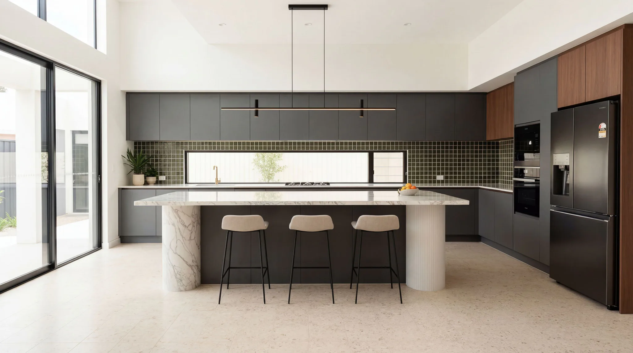Contemporary kitchen featuring a large marble-topped island with three beige bar stools, black cabinetry with green tile backsplash, stainless steel appliances, and pendant lighting above.