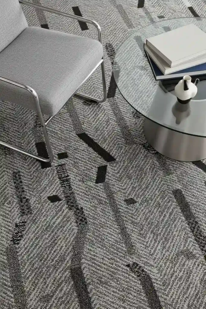 Grey herringbone pattern carpet with black accents, featuring a modern chair and glass coffee table.